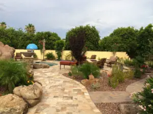 Beautifully landscaped backyard featuring a stone pathway, lush greenery, comfortable seating areas, and a small pool with a water feature.