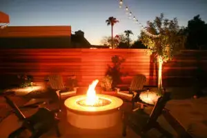 Cozy backyard fire pit area with Adirondack chairs, surrounded by string lights and a modern wooden fence, creating a warm evening ambiance.