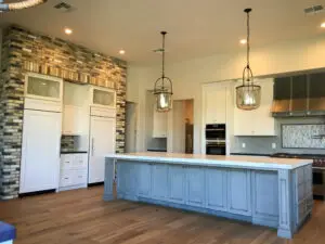 Spacious kitchen with white cabinets, a large island with a blue base, and rustic brick accents.