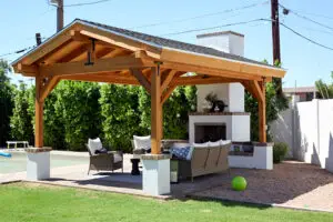 Cozy outdoor patio with a wooden pavilion, featuring a stone fireplace, comfortable seating, and a lush green lawn.