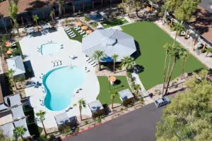 Aerial view of a resort-style swimming pool area with palm trees, lounge chairs, and a pavilion surrounded by landscaped greenery.