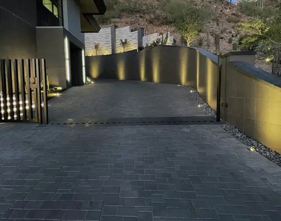 Evening view of a luxurious hillside driveway with interlocking pavers, illuminated by subtle landscape lighting, leading to a modern home.