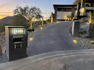 Illuminated driveway with modern pavers leading up to a luxury hillside home, featuring built-in landscape lighting and a sleek mailbox.