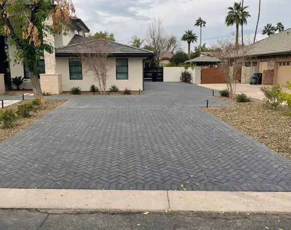 Modern paver driveway in a residential area featuring a sleek herringbone pattern, surrounded by minimalist landscaping