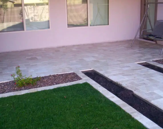 Freshly laid stone patio with surrounding grass and planting beds, featuring a garden swing set.