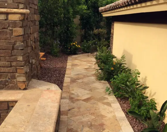 Stone pathway surrounded by lush greenery and stone walls, leading to a beautifully designed patio area.