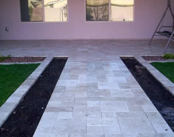 Newly paved patio area with natural stone tiles, bordered by freshly planted grass and soil beds, ready for planting.