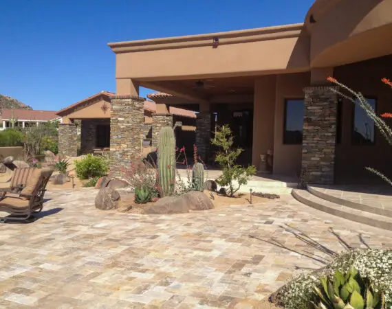 Elegant patio area with stone pillars, desert landscaping, and seating, framed by natural stone pavers and a clear blue sky.