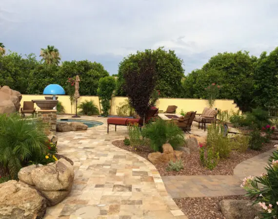 Beautifully landscaped backyard featuring a stone pathway, lush greenery, comfortable seating areas, and a small pool with a water feature.