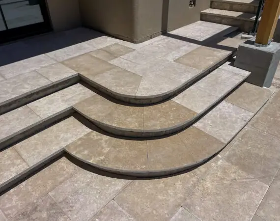 Elegant tiered stone steps with clean lines and smooth curves, leading up to a patio area with matching stone flooring.