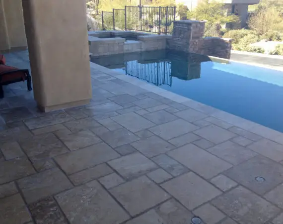 Stylish infinity pool with natural stone-tiled decking, shaded by columns, offering a serene view of the landscape.