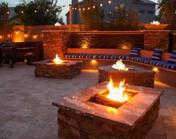 Outdoor patio area with multiple fire pits, comfortable seating, string lights, and a built-in grill, creating a warm and inviting atmosphere for evening gatherings.