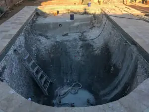 Unfinished swimming pool with a ladder and construction equipment inside, surrounded by newly installed pool decking.