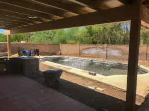 Covered patio area overlooking a backyard construction site with an unfinished swimming pool and scattered building materials.