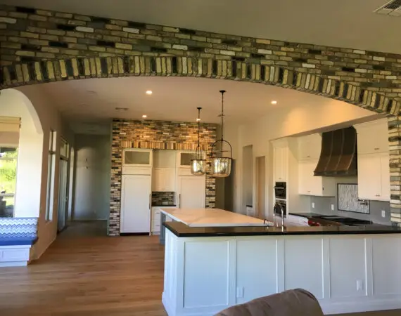 Spacious kitchen with brick archway, white cabinets, stainless steel appliances, and a large marble island with pendant lighting.