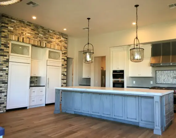 Spacious kitchen with white cabinets, a large island with a blue base, and rustic brick accents.