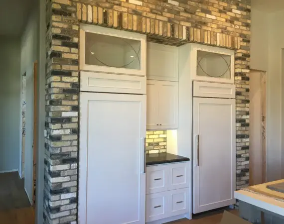 Sleek white kitchen cabinets with built-in appliances, surrounded by a rustic brick archway.