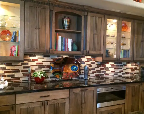 Modern kitchen featuring wooden cabinets, a stylish backsplash, and decorative items including colorful art pieces, books, and a small potted plant.