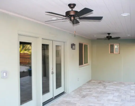 Modern patio with double glass doors, ceiling fans, a wall-mounted light, and a tiled floor.