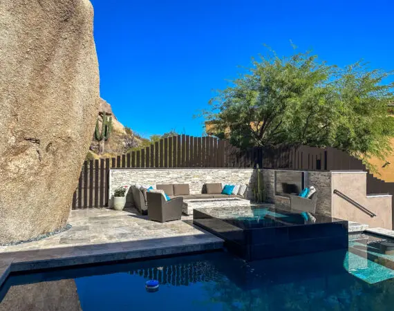 Contemporary pool area with a sleek infinity pool, built-in seating, and modern outdoor furniture set against a dramatic rock backdrop.