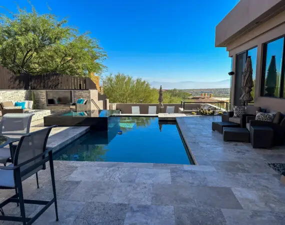 Modern backyard pool area featuring an infinity pool with a stunning view, lounge seating, and a sleek outdoor dining space on a tiled patio.