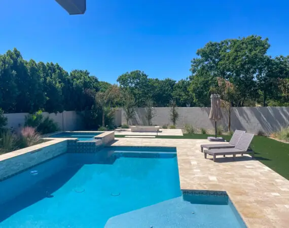 Luxurious backyard pool area with a spacious deck, comfortable loungers, and a raised spa, surrounded by lush greenery and a privacy wall.