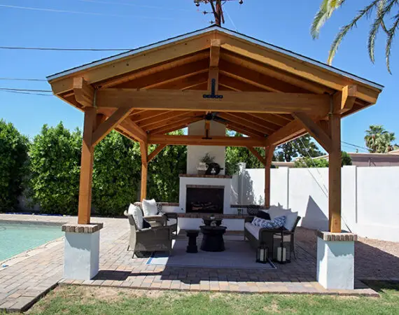 Beautiful outdoor space with a wooden pavilion, stone fireplace, and comfortable seating near a pool.