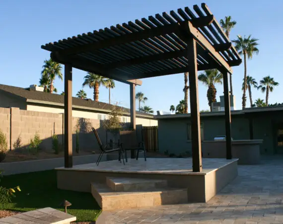 Elevated patio with a wooden pergola and outdoor furniture, surrounded by palm trees and desert landscape.