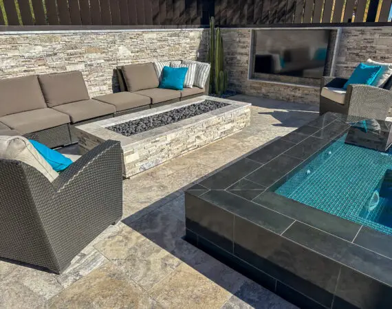 Modern outdoor spa with a sleek black tiled edge, comfortable seating area, and a stone fire pit.