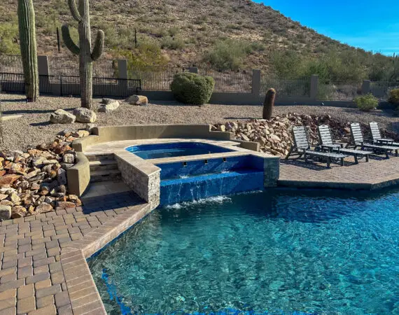 Beautiful desert-themed outdoor spa with a waterfall feature, stone surroundings, and lounge chairs for relaxation.