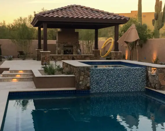 Luxurious outdoor spa with a stone waterfall feature and a shaded seating area, perfect for relaxation.