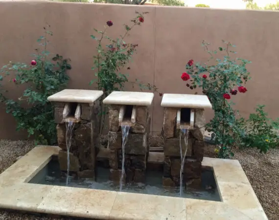 Triple stone water feature with rose bushes in a serene backyard setting.