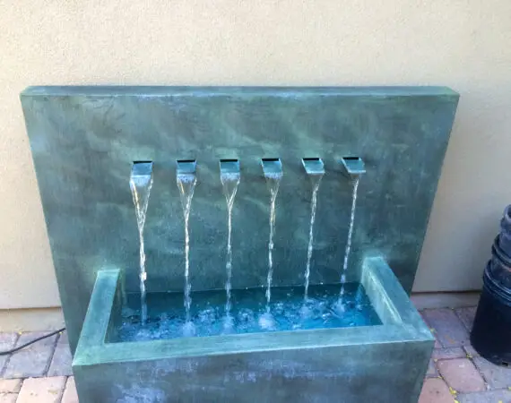 Modern backyard water feature with six streams flowing into a rectangular basin, designed with a sleek concrete finish.