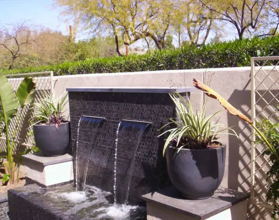 Elegant backyard water feature with dual waterfalls and potted plants, adding a touch of tranquility to the outdoor space.