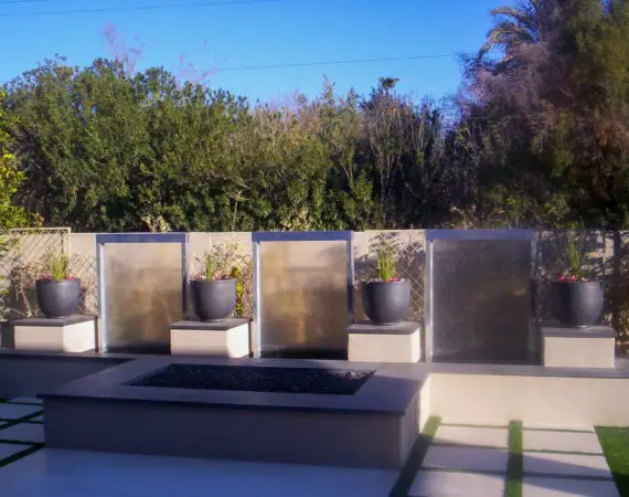 Contemporary backyard water feature with three glass panels and stylish potted plants, enhancing outdoor aesthetics.