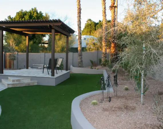 A landscaped backyard with a wooden pergola, synthetic turf, a desert garden with native plants, and a swimming pool.