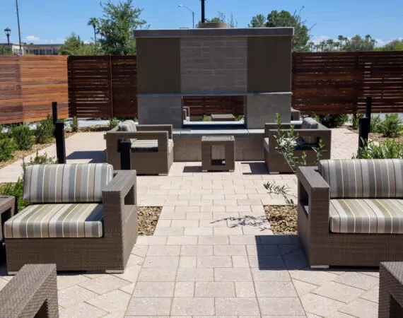 Outdoor seating area in an apartment property space with comfortable wicker chairs and a central fireplace, surrounded by plants and wooden fencing.