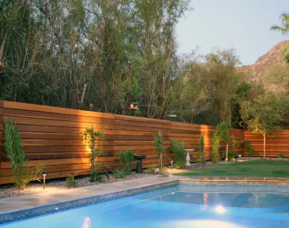 Backyard pool area with a wooden fence, lush greenery, and mountain views in the background.