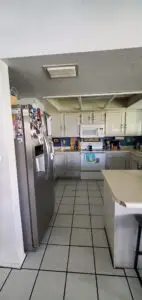 Modern kitchen with white cabinetry, stainless steel appliances, and white tile floors. The refrigerator is covered with family photos and magnets.