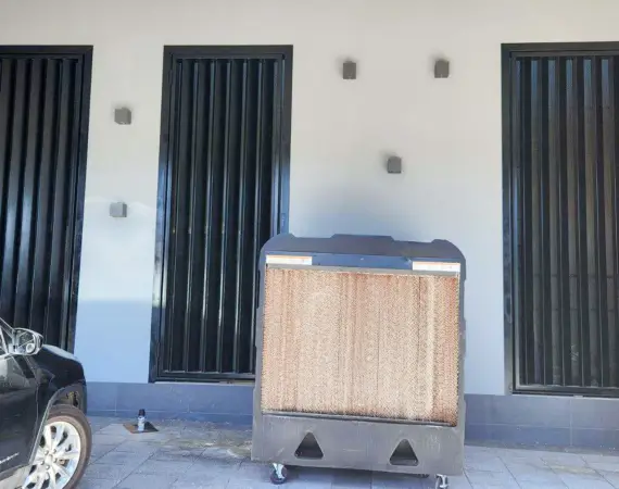 Black metal security bars on three windows of a white building, with an industrial evaporative cooler in front.