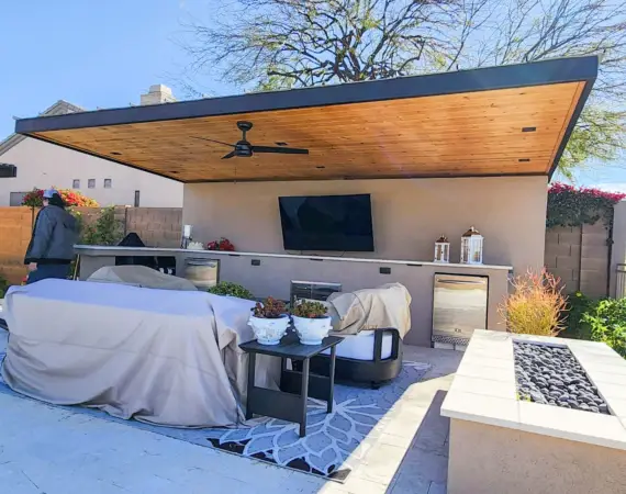 Modern outdoor living space with a covered patio, built-in TV, seating area, and outdoor kitchen, designed for comfort and entertainment.