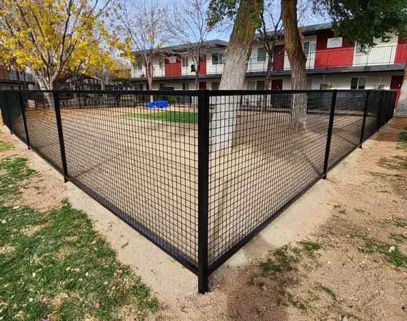 Black metal mesh fence enclosing a landscaped area with trees, providing security and aesthetic appeal in an apartment complex.