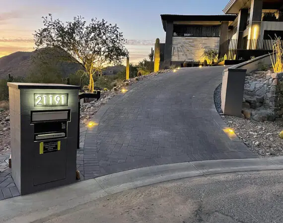 Illuminated driveway with modern pavers leading up to a luxury hillside home, featuring built-in landscape lighting and a sleek mailbox.