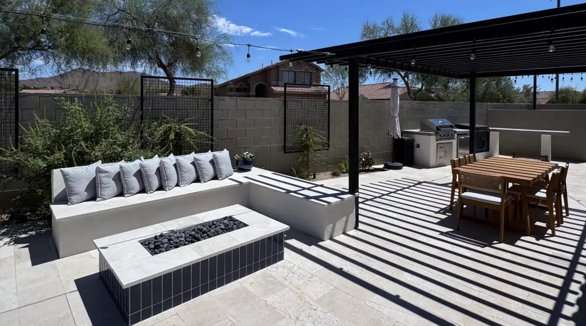 Modern outdoor kitchen with a stainless steel grill and side burner set on a stone countertop, surrounded by a stylish, curved concrete base.