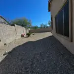 Bare side yard with gravel ground and minimal landscaping, providing a blank slate for future outdoor design and enhancements.