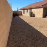 Side yard with gravel and an air conditioning unit, along a block wall and stucco house, offering a blank area for future landscaping.