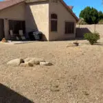 Gravel-covered backyard with sparse landscaping and patio area, adjacent to a stucco house, showing an open space ready for redesign.